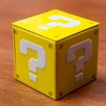Yellow cube with white question marks on a wooden surface