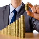 Businessman stacking gold coins to symbolise financial growth and savings.