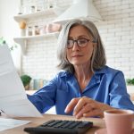 Mature woman reviewing property bills with calculator at home office