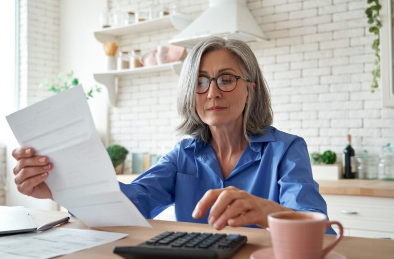 Mature woman reviewing property bills with calculator at home office