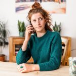 Woman sitting at a table on a phone call, looking concerned about a housing issue