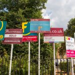 Multiple estate agent boards showing properties for sale, sold, and to let in a UK street.