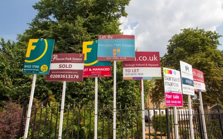 Multiple estate agent boards showing properties for sale, sold, and to let in a UK street.
