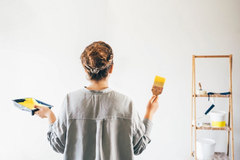 Rear view of a woman with paint brush painting a wall