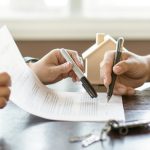 Two people signing a rental agreement with house keys and a model home on the table.