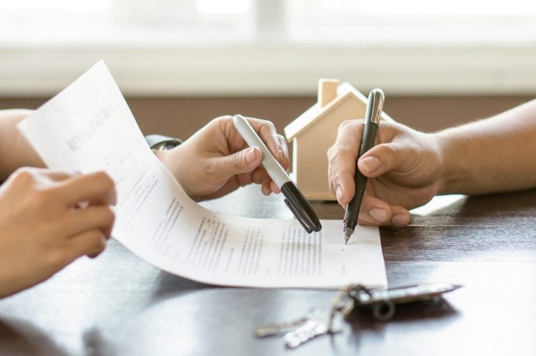Two people signing a rental agreement with house keys and a model home on the table.