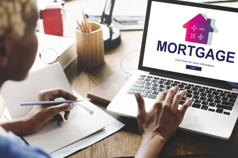 Person researching mortgage options on a laptop while taking notes