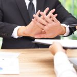 A businessman crossing hands infront of him and a person sitting opposit passing papers to sign