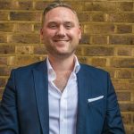 Property auctioneer in business attire standing against a brick wall
