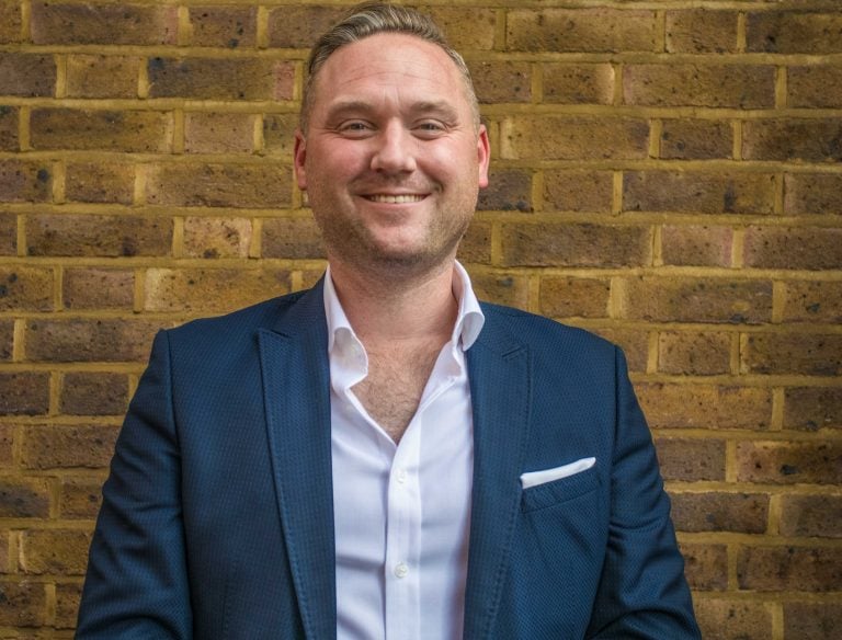 Property auctioneer in business attire standing against a brick wall