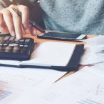 Person calculating housing expenses with receipts, calculator, and financial documents.