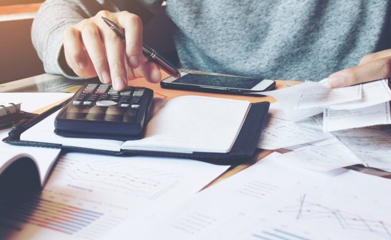 Person calculating housing expenses with receipts, calculator, and financial documents.