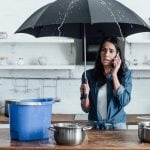 Woman on phone under umbrella in kitchen during water leak