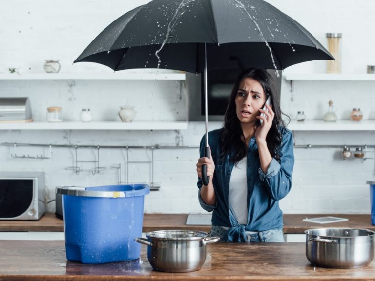 Woman on phone under umbrella in kitchen during water leak