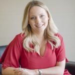 Woman in red dress smiling while seated in an office chair.