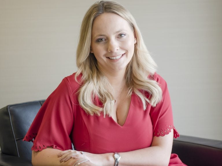 Woman in red dress smiling while seated in an office chair.