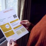 Person holding an energy bill while reviewing household energy costs.