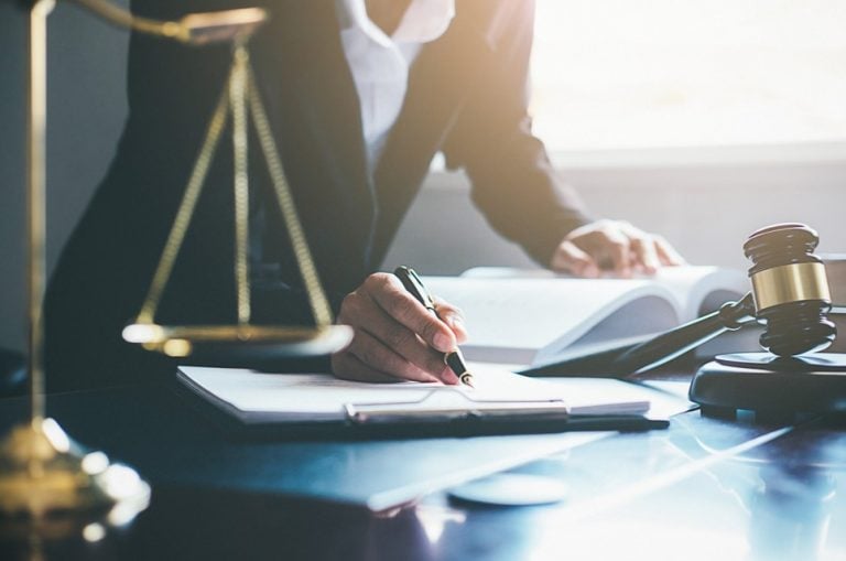 Lawyer writing notes at desk with legal scales and gavel.