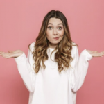 Portrait of a confused young casual girl shrugging shoulders isolated over pink background
