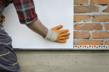 Worker placing styrofoam, polystyrene thermal insulation to brick wall, house renovation