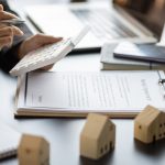 Person reviewing roof repair costs and housing documents at a desk with miniature house models