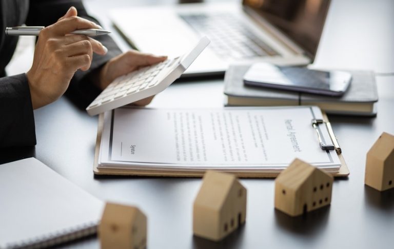 Person reviewing roof repair costs and housing documents at a desk with miniature house models