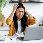 A women at a laptop in a kitchen with her hands on her head in frustration