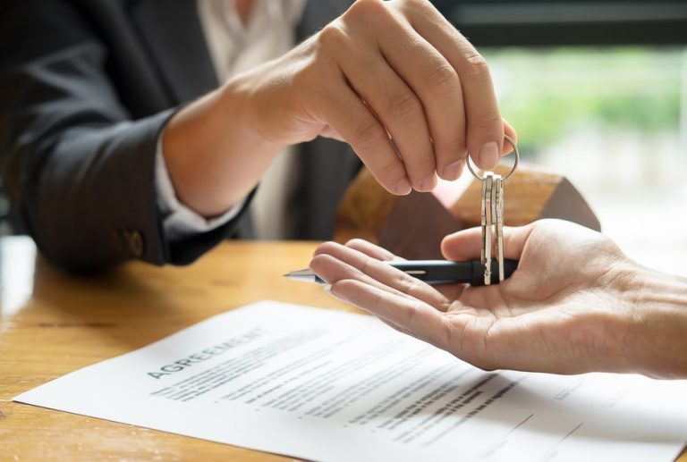Hands handing over keys with renters agreement paperwork on a table