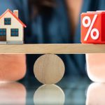 House and percentage symbol balanced on wooden seesaw representing mortgage rates.