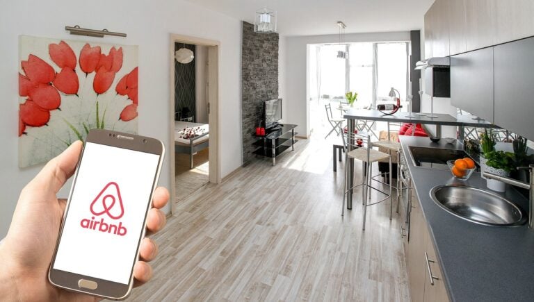 Person holding smartphone with Airbnb app in modern short-let apartment kitchen and living area