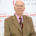 Chris Daniel receiving an award in front of the sponsor's board wearing a suit, shirt and tie