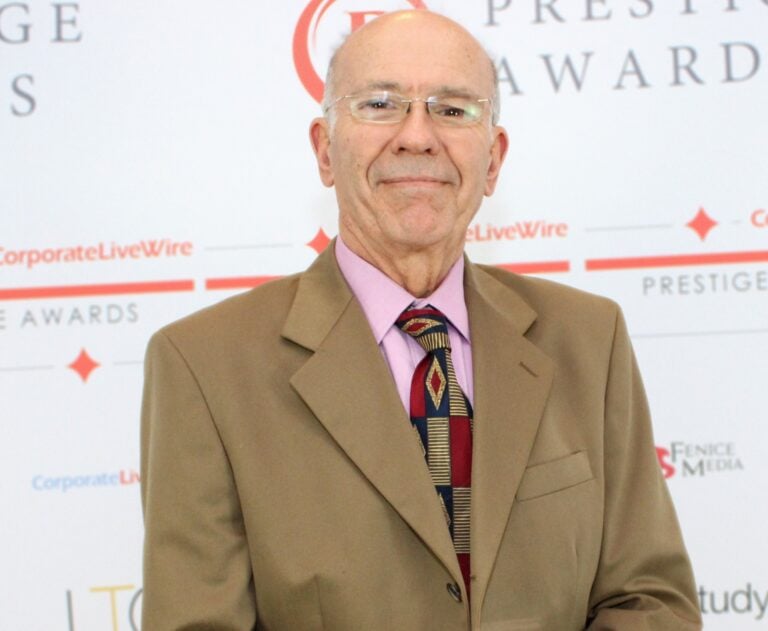 Chris Daniel receiving an award in front of the sponsor's board wearing a suit, shirt and tie