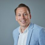 Business professional in light blue blazer smiling against grey background