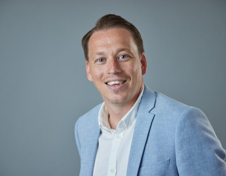 Business professional in light blue blazer smiling against grey background