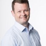 Smiling professional in light blue shirt representing property and insurance industry.
