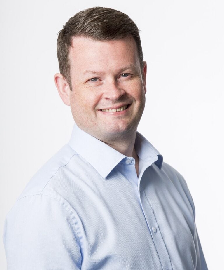 Smiling professional in light blue shirt representing property and insurance industry.