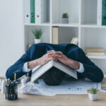 Overwhelmed landlord with head on desk surrounded by property documents and charts