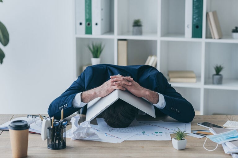 Overwhelmed landlord with head on desk surrounded by property documents and charts