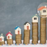 Rising house prices compared to income growth shown with houses on stacked coins