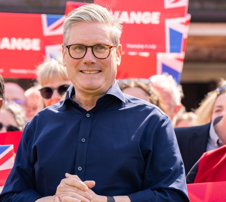 Keir Starmer at a Labour campaign event with supporters holding red signs and Union Jack flags