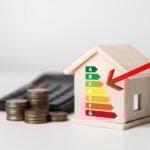 Wooden house model with EPC rating chart and red arrow beside stacked coins and calculator