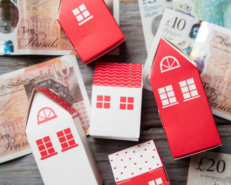 Paper houses displayed on top of UK banknotes to illustrate funding pressures on social housing
