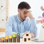 Landlord stressed over property costs and EPC ratings while money flows from laptop.