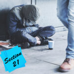 Person sitting on the street beside a cup as Section 21 eviction concept is highlighted