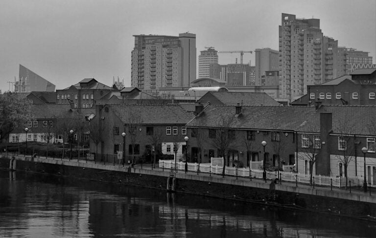 Salford riverside homes with modern high-rises in the background on an overcast day.