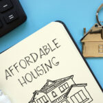 Notebook labeled “Affordable Housing” beside calculator and house-shaped keyring symbolizing housing costs.