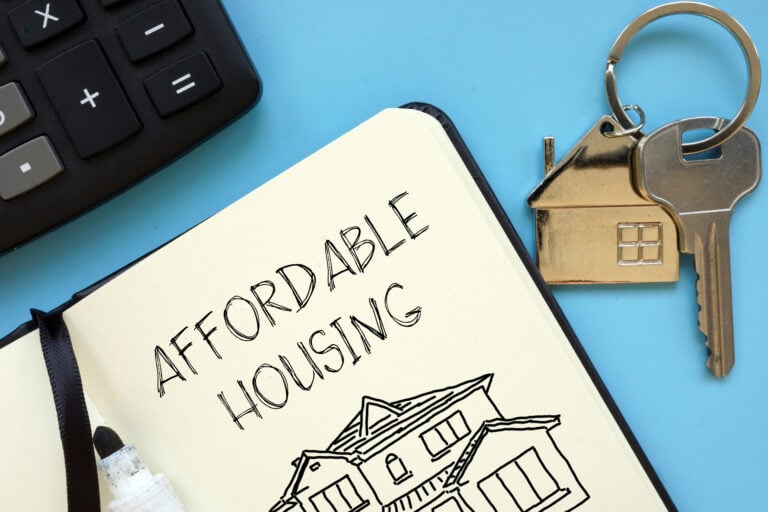 Notebook labeled “Affordable Housing” beside calculator and house-shaped keyring symbolizing housing costs.