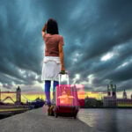 Traveller with suitcase overlooking Tower Bridge and London skyline at sunset