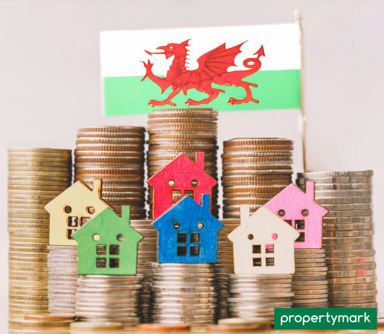 Stacks of coins with colourful house icons and Welsh flag symbolising rising housing costs in Wales