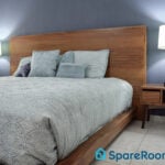 Modern bedroom with wooden bed frame and soft blue bedding representing spare room rental potential